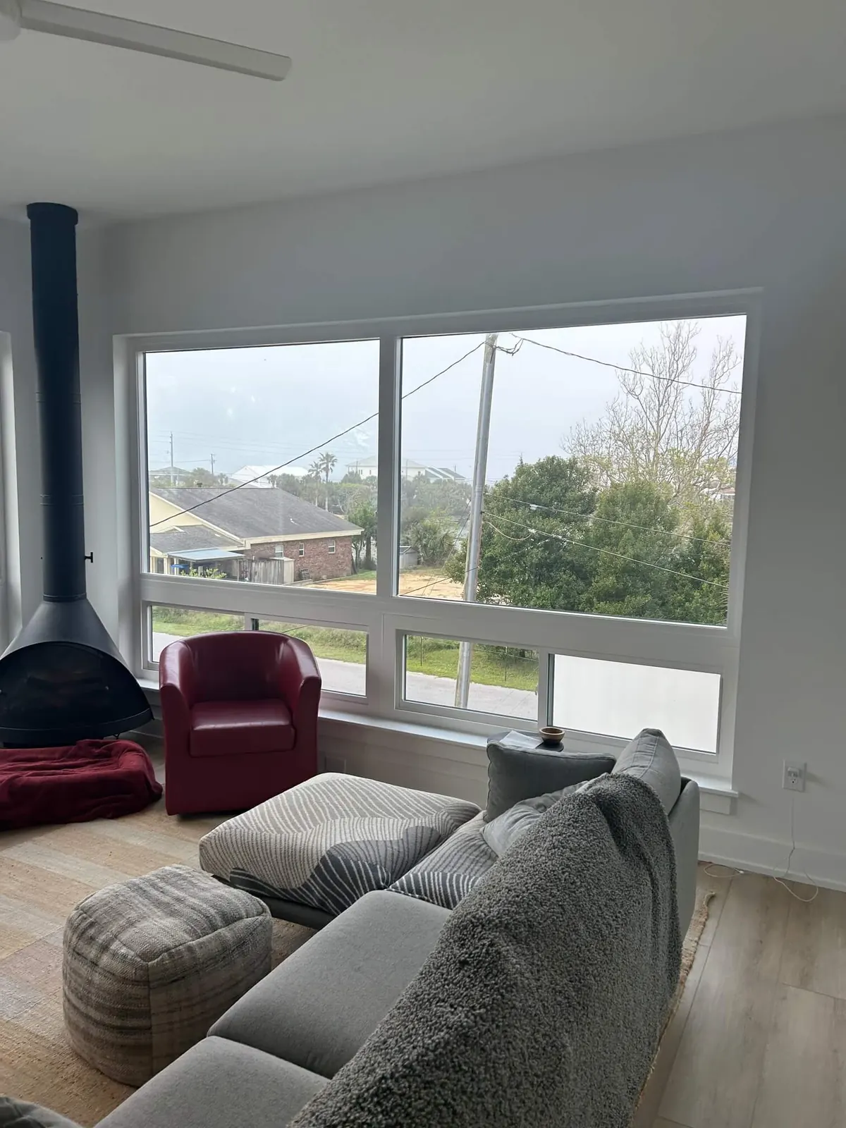 Living room with a large white-framed picture window above a row of smaller windows, next to a black hanging fireplace and a red armchair.